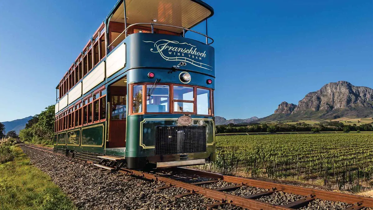 Open-sided Franschhoek wine tram rolling past vineyards on a hop-on hop-off day from Cape Town